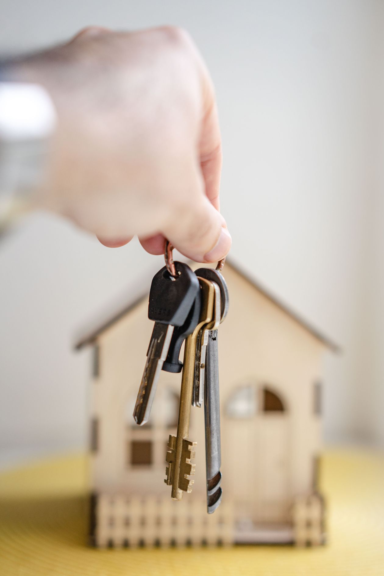 Hand holding house keys with a miniature wooden house in the background